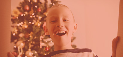 Young boy looking into box with a christmas tree behind him.